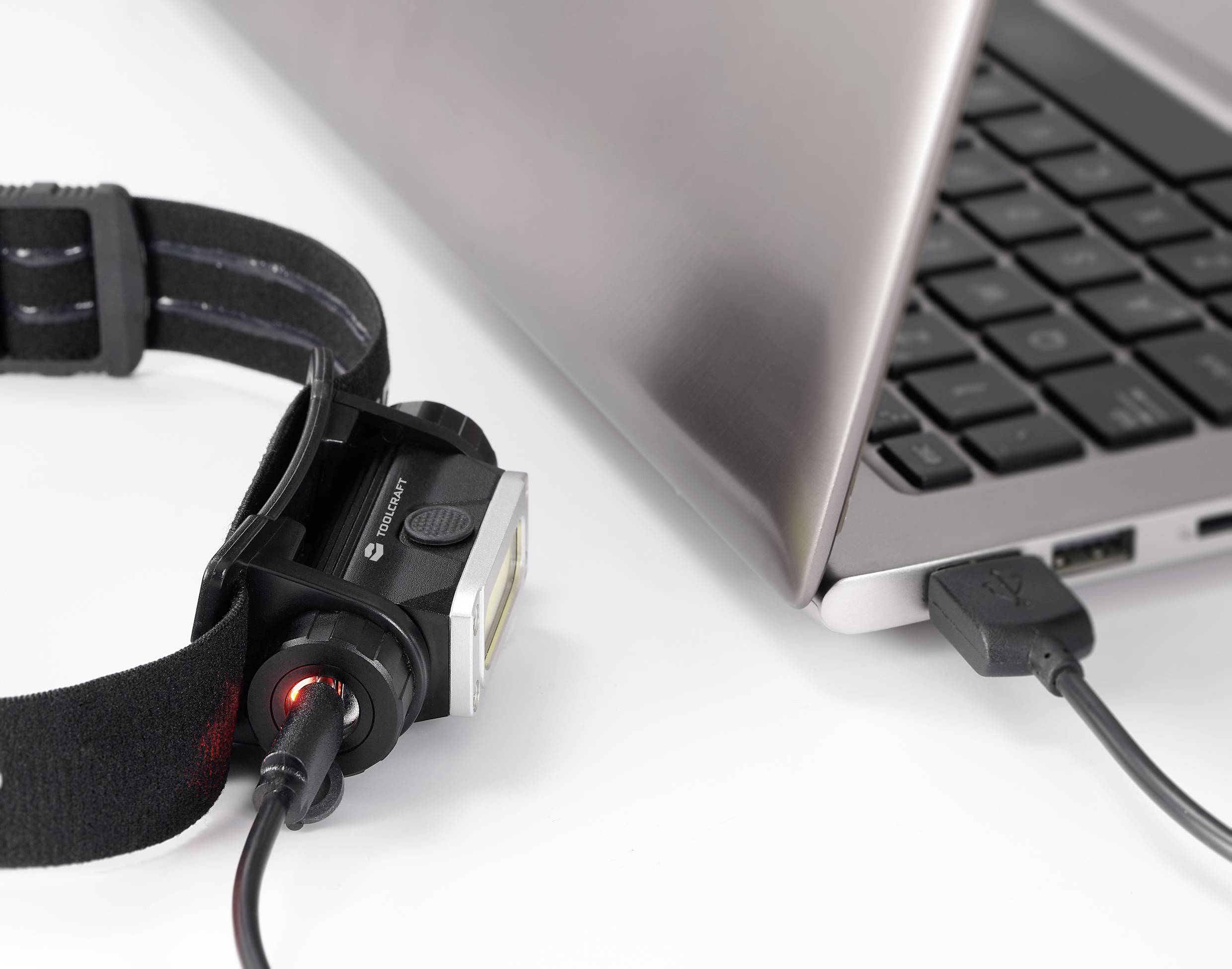 Una lampada frontale viene collegata a un laptop tramite un cavo USB per la ricarica. Il laptop è aperto.