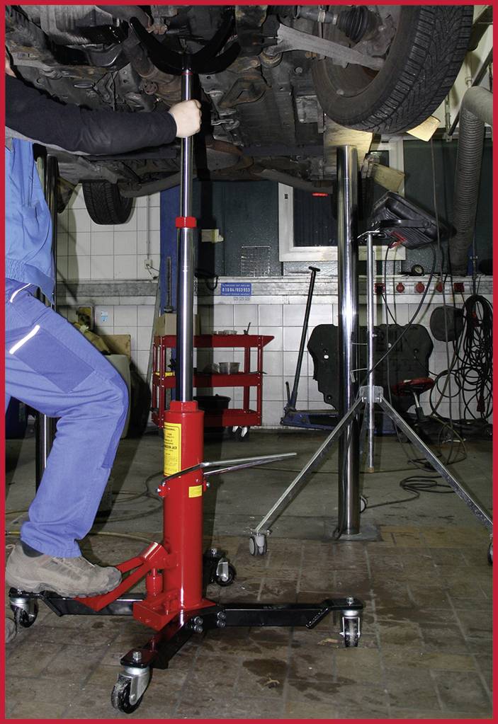 'Meccanico ripara veicolo su ponte sollevatore' – Una persona in tuta da lavoro blu sta lavorando su un'auto sollevata su un ponte sollevatore.