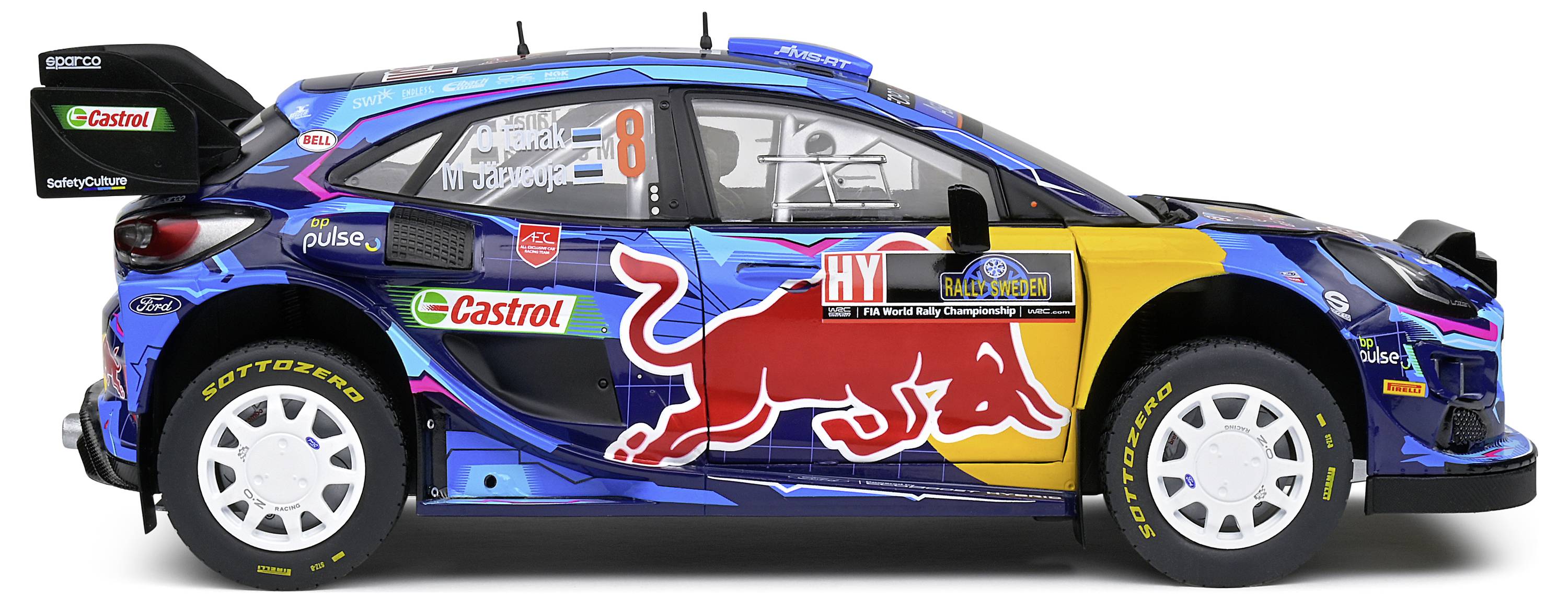 Un'auto da rally con verniciatura blu, gialla e rossa, sponsorizzata da Red Bull e Castrol, è parcheggiata di lato. Numero di gara '8'.
