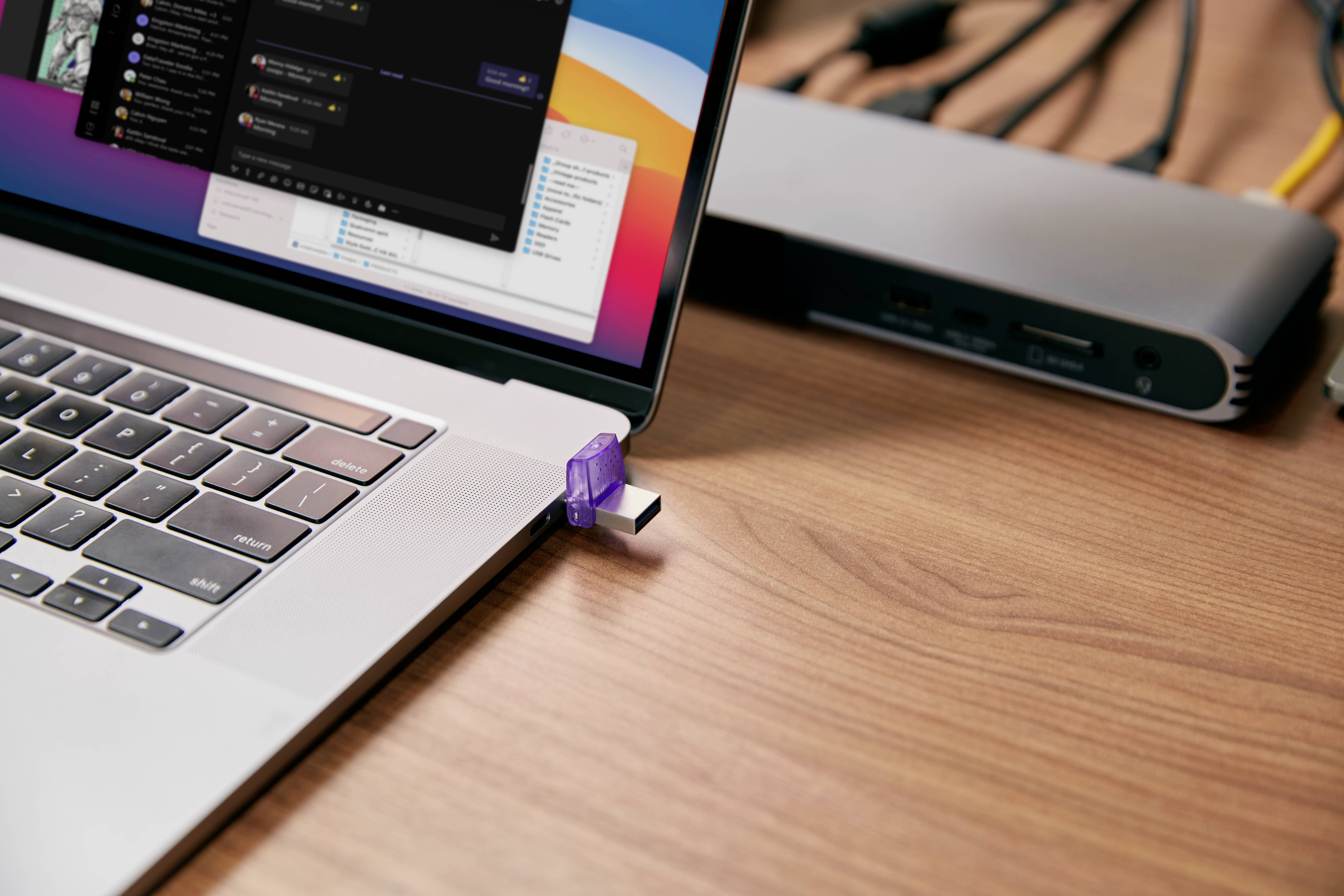 Un laptop con una chiavetta USB inserita in una porta USB. Sullo sfondo sono visibili cavi e un dock.