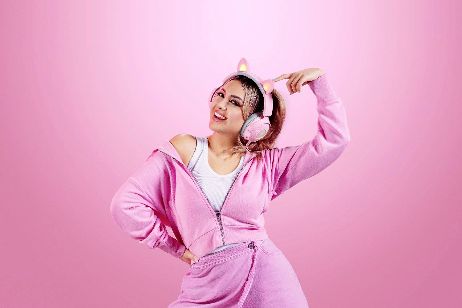 Donna in abbigliamento casual rosa che danza sullo sfondo rosa, indossa cuffie a forma di orecchie di gatto e sorride, incarnando gioia e spensieratezza.