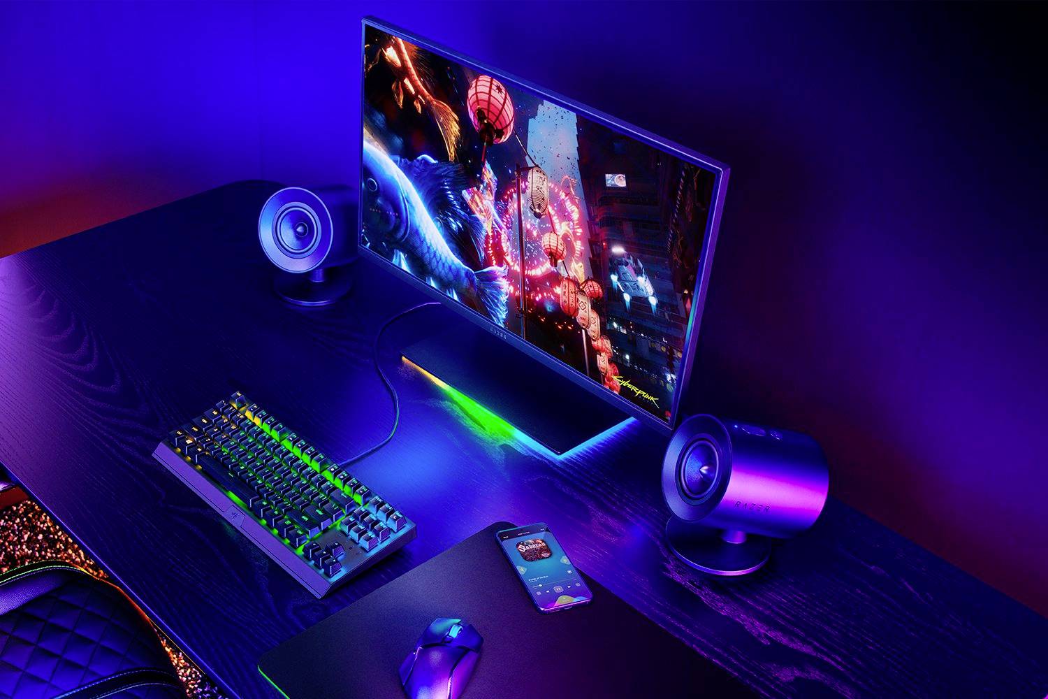 Postazione computer su un tavolo con illuminazione LED arcobaleno, un monitor, una tastiera, un mouse e altoparlanti; pronti per giocare.