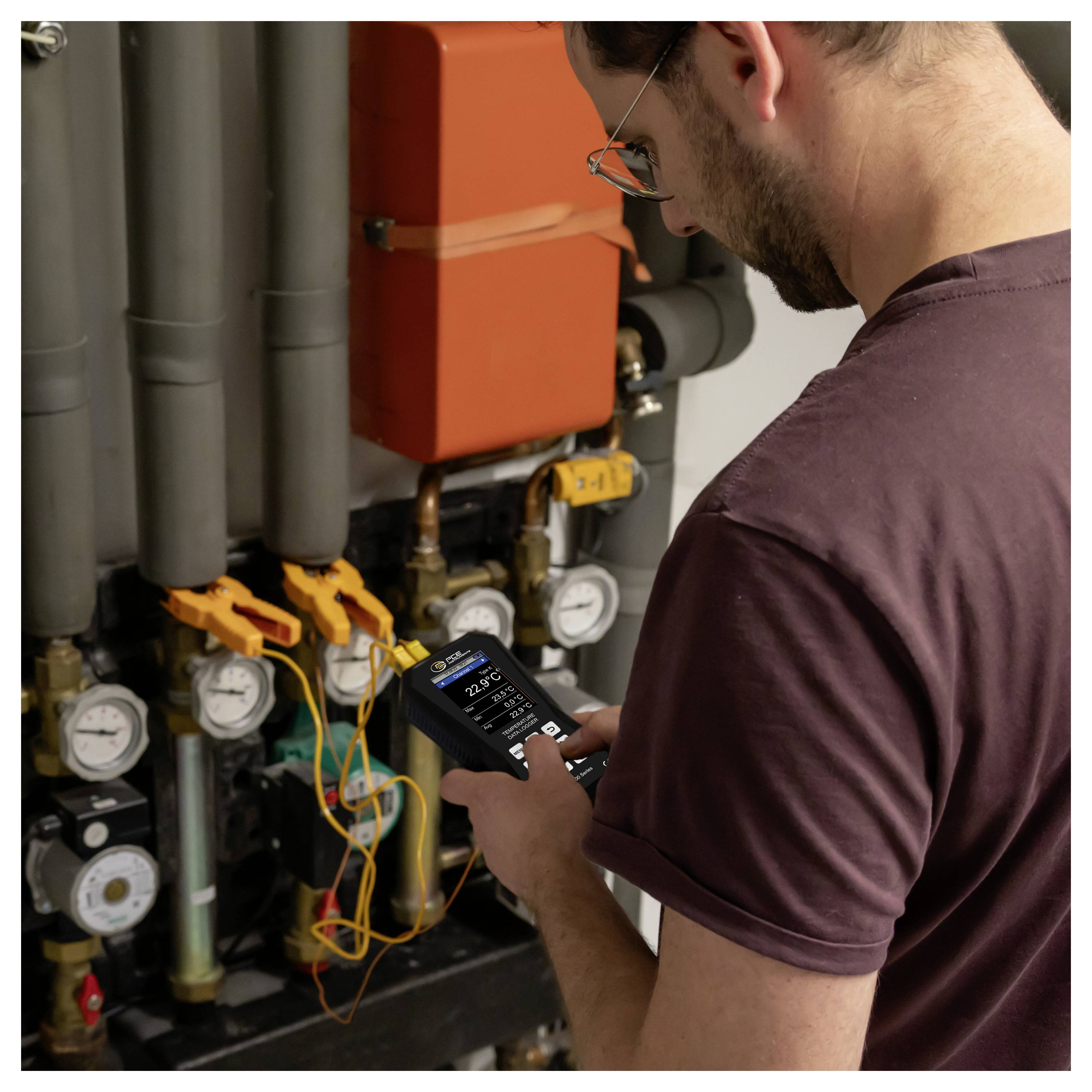Tecnico che ispeziona i controlli del sistema di riscaldamento con un misuratore portatile, controllando tubazioni, manometri e cablaggio all'interno di una sala tecnica.