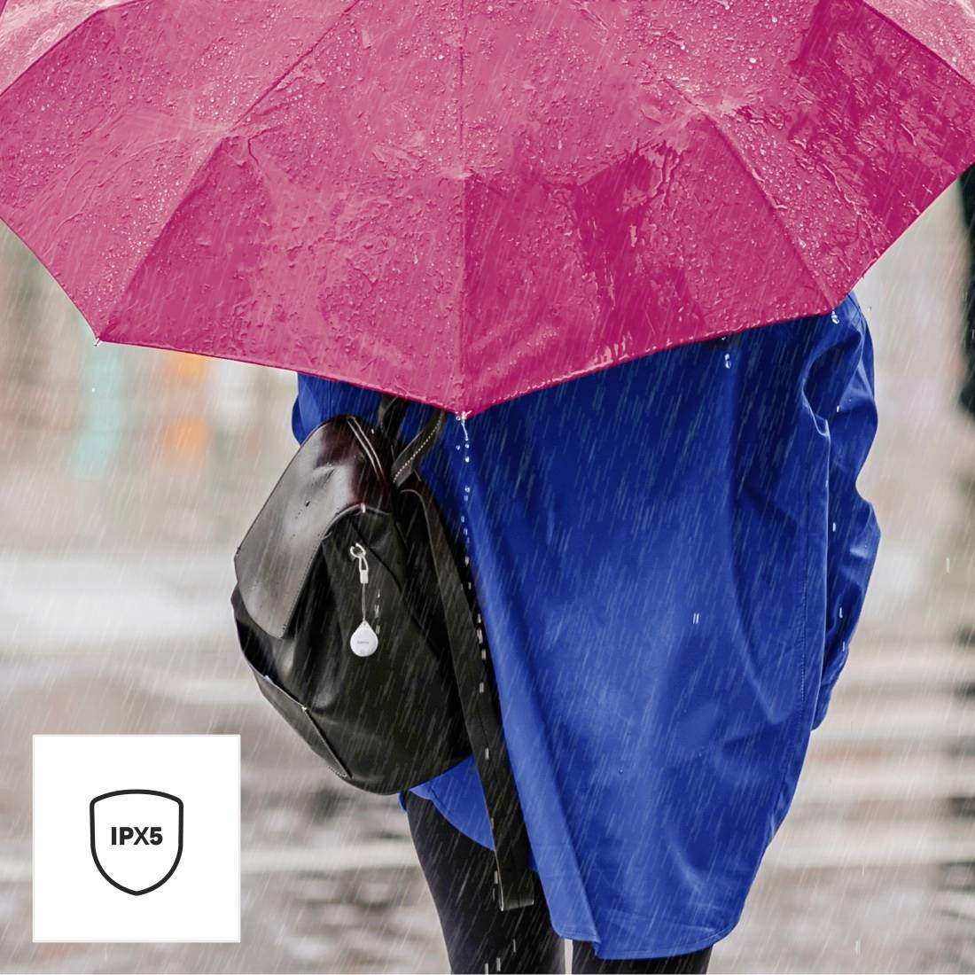 Una persona con un ombrello rosa cammina sotto la pioggia. Sullo sfondo è visibile uno zaino. Nell'immagine è presente un simbolo 'IPX5'.