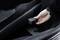 Una mano tiene un piccolo oggetto nero nel bagagliaio di un'auto. L'oggetto sembra essere un accessorio o un attrezzo.
