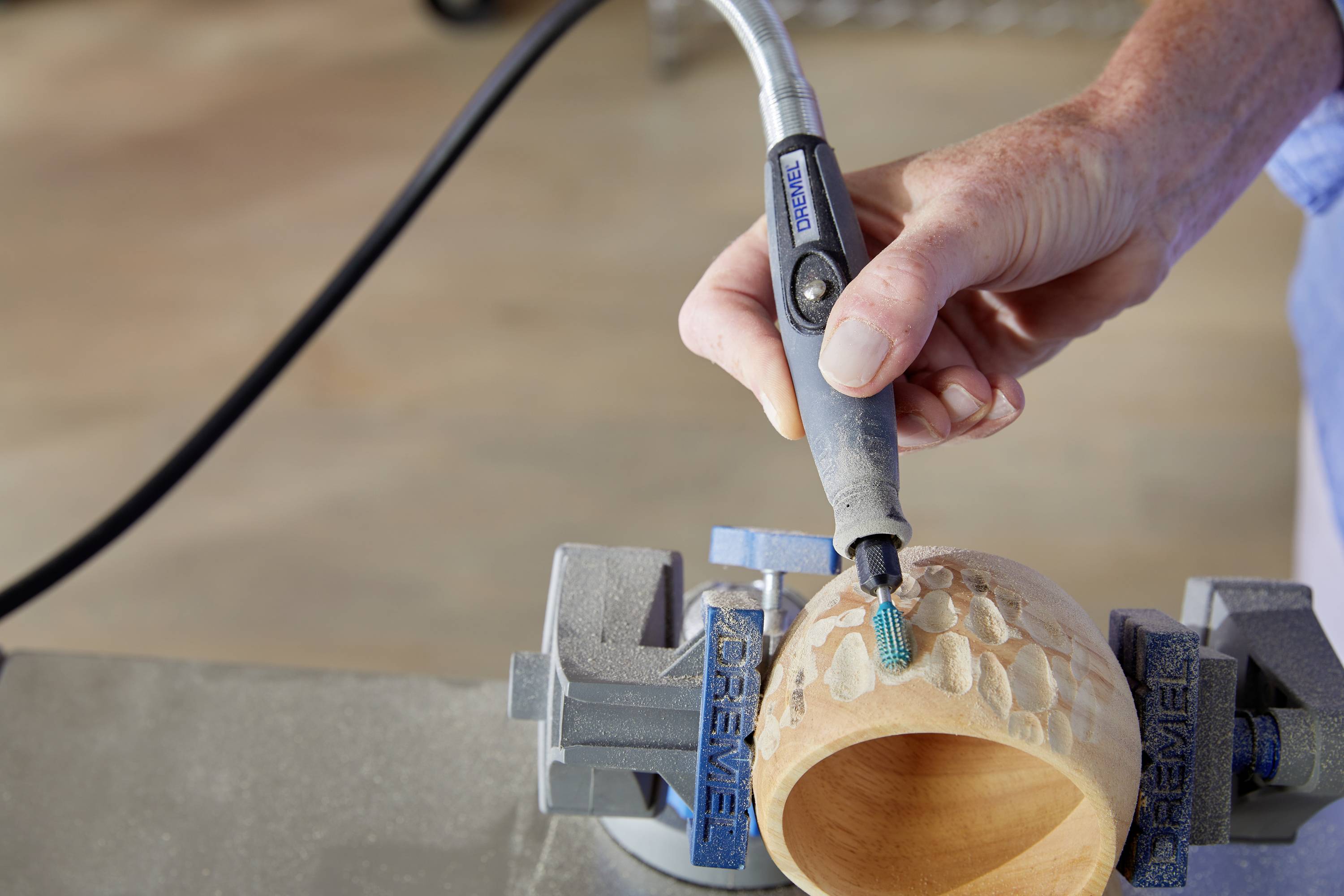 'Una mano utilizza un utensile rotante per lavorare un oggetto di legno in un laboratorio.'