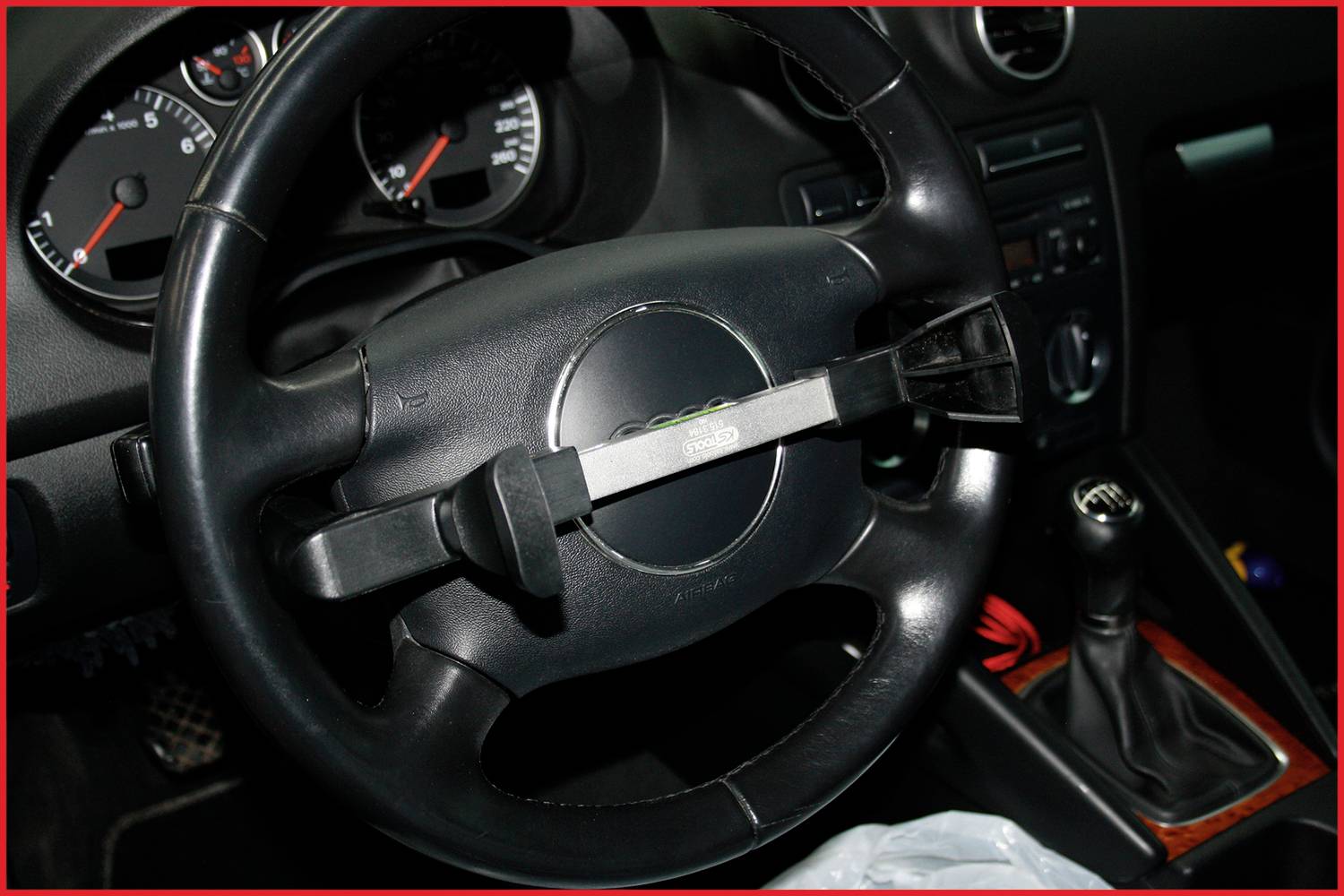 Bloccasterzo installato nell'auto. Il volante mostra il cruscotto con tachimetro e leva del cambio sullo sfondo.
