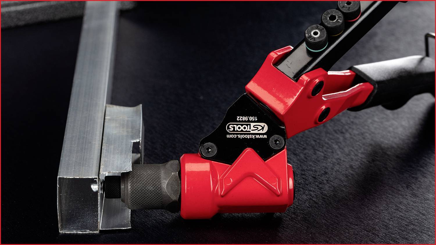 Un utensile per rivetti con impugnatura rossa inserisce un rivetto in un profilo metallico. Lo strumento reca la scritta 'KS TOOLS'.