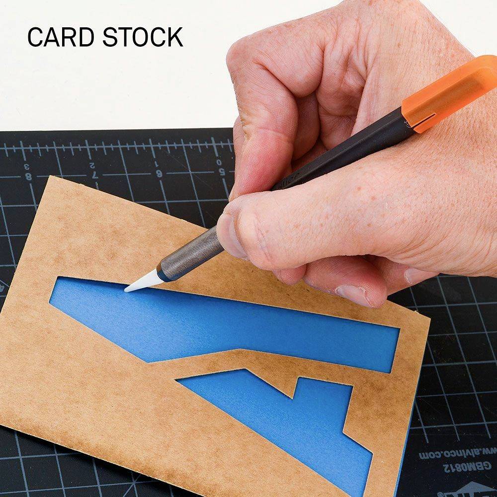 Una mano taglia un modulo su carta da cartoncino con un coltello. In alto a sinistra è scritto 'CARD STOCK'.