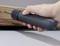 Una mano tiene un cacciavite elettrico che avvita una vite in una tavola di legno. Il cacciavite è grigio scuro.