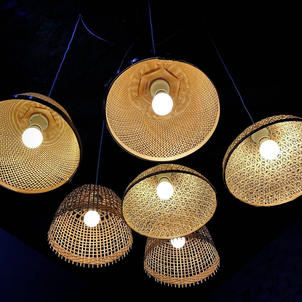 Sei lampadari a sospensione con paralumi intrecciati in materiali naturali illuminano calorosamente un ambiente buio.