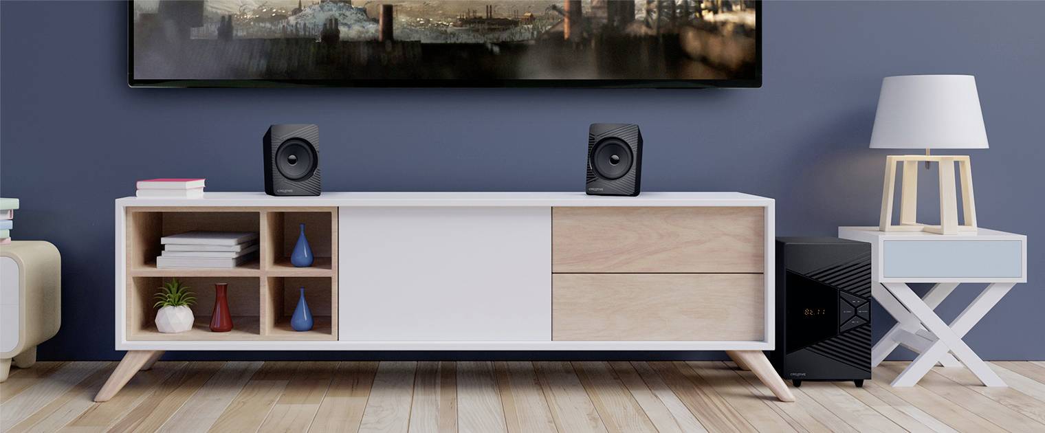 Un soggiorno moderno con un mobile TV bianco, su cui sono posizionati due altoparlanti. Accanto un comodino con una lampada. Sullo sfondo una vista della città.