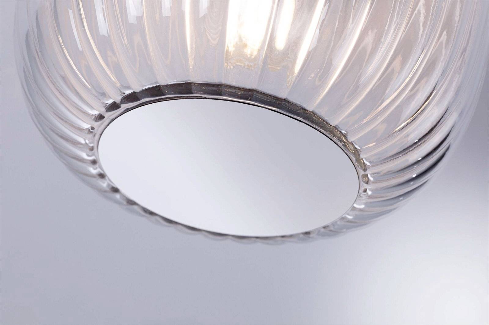 Una lampada a sospensione rotonda e scanalata in vetro risplende con calore e dolcezza, illuminando un ambiente minimale e moderno.