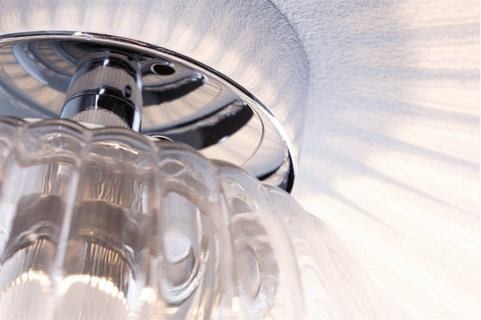 Primo piano di una lampada da soffitto decorativa in vetro con dettagli argentati che proietta una luce morbida e raggiante verso l'alto.