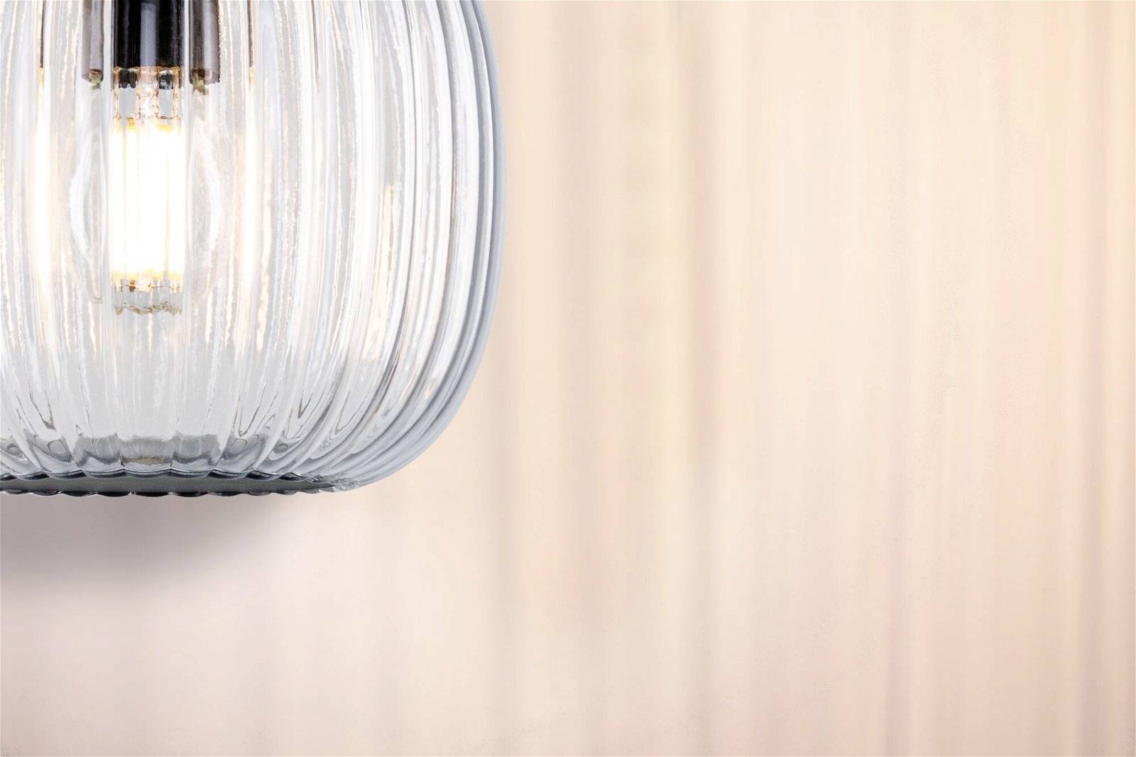 Una lampada elegante con vetro scanalato illumina con calore su uno sfondo chiaro.