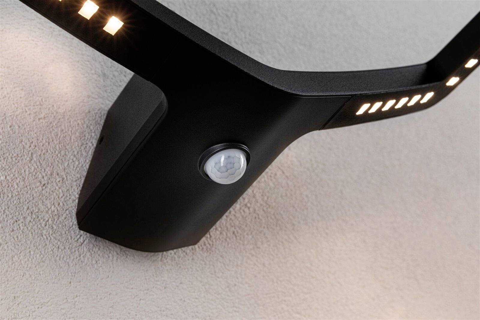 Una moderna lampada da esterno nera con sensore di movimento integrato, montata a parete. Emana luce verso il basso e lateralmente.