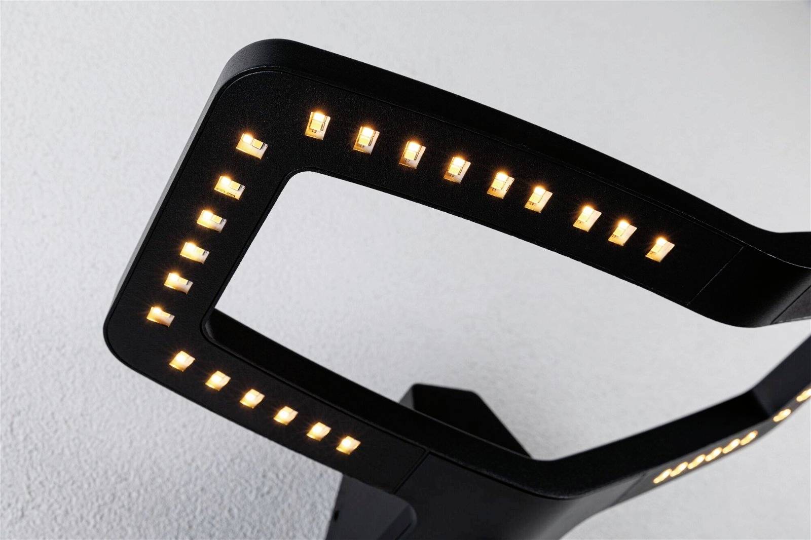 Moderna lampada LED nera dalle forme sinuose, illumina con numerose piccole luci su una parete chiara.
