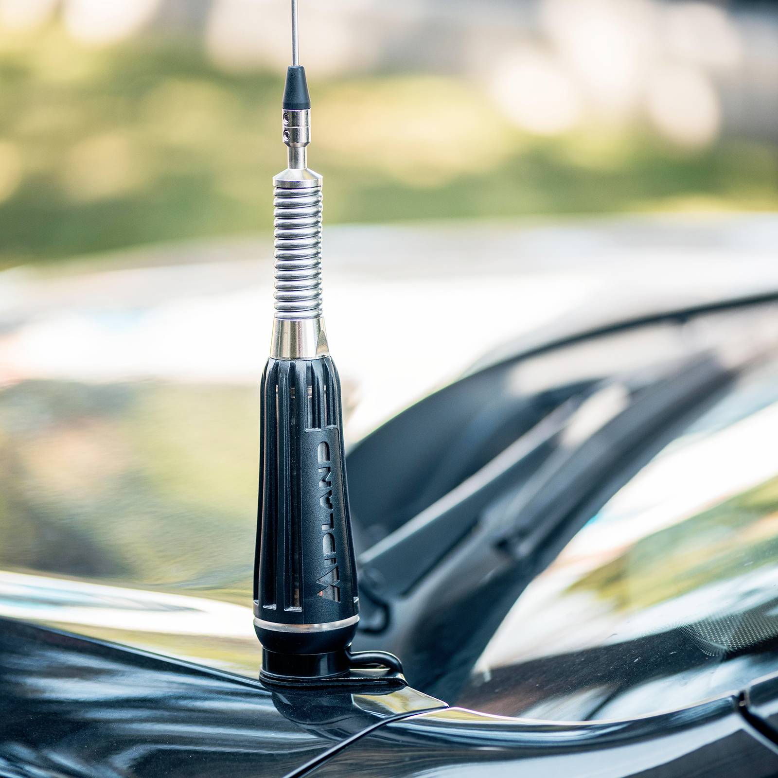Un'antenna per auto con una molla metallica e una base nera è montata sul cofano di un veicolo.