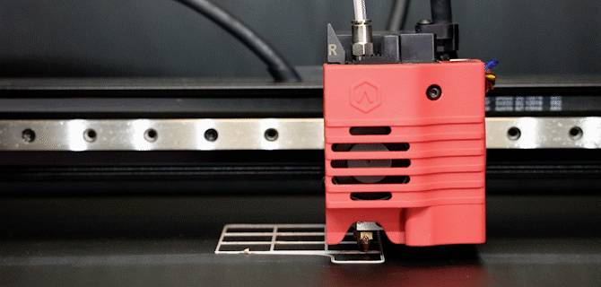 Una stampante 3D sta stampando un pattern a griglia rettangolare su una superficie piana. La testina di stampa è rossa e in movimento.