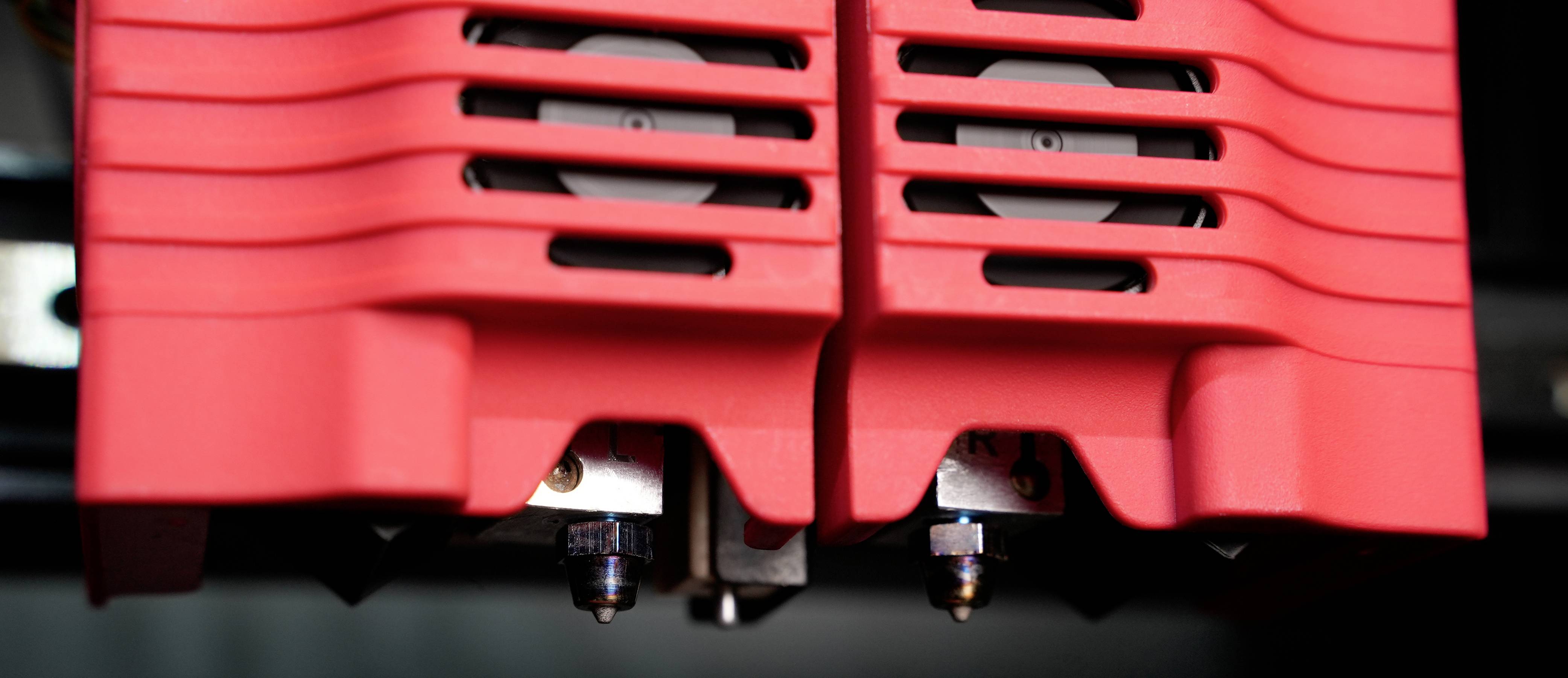 Primo piano di due estrusori di una stampante 3D rivestiti in rosso, montati strettamente l'uno accanto all'altro.
