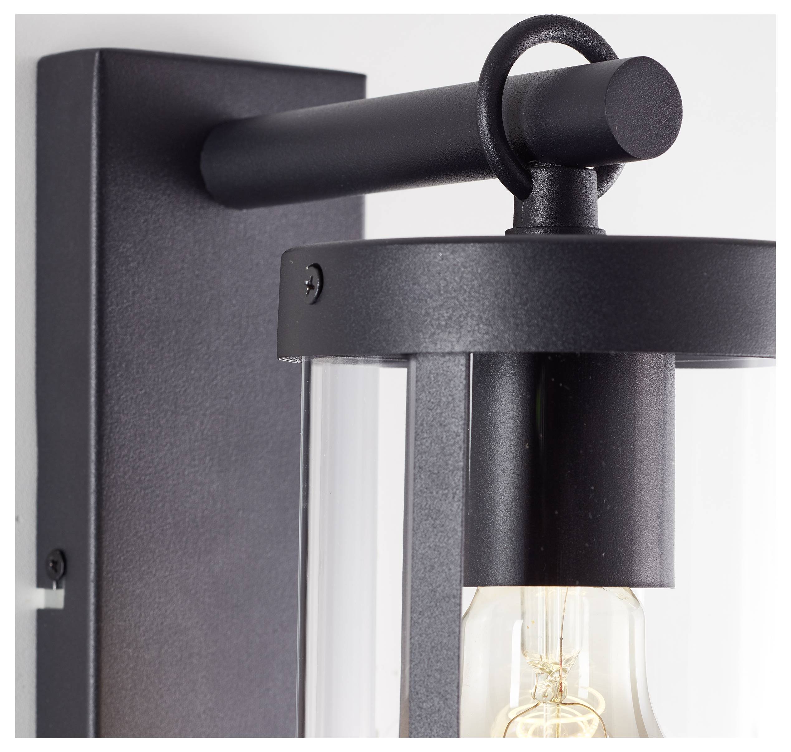 Applique da parete nera in metallo con capsula di vetro trasparente intorno alla lampadina. Design moderno e minimalista, montata su una parete bianca.