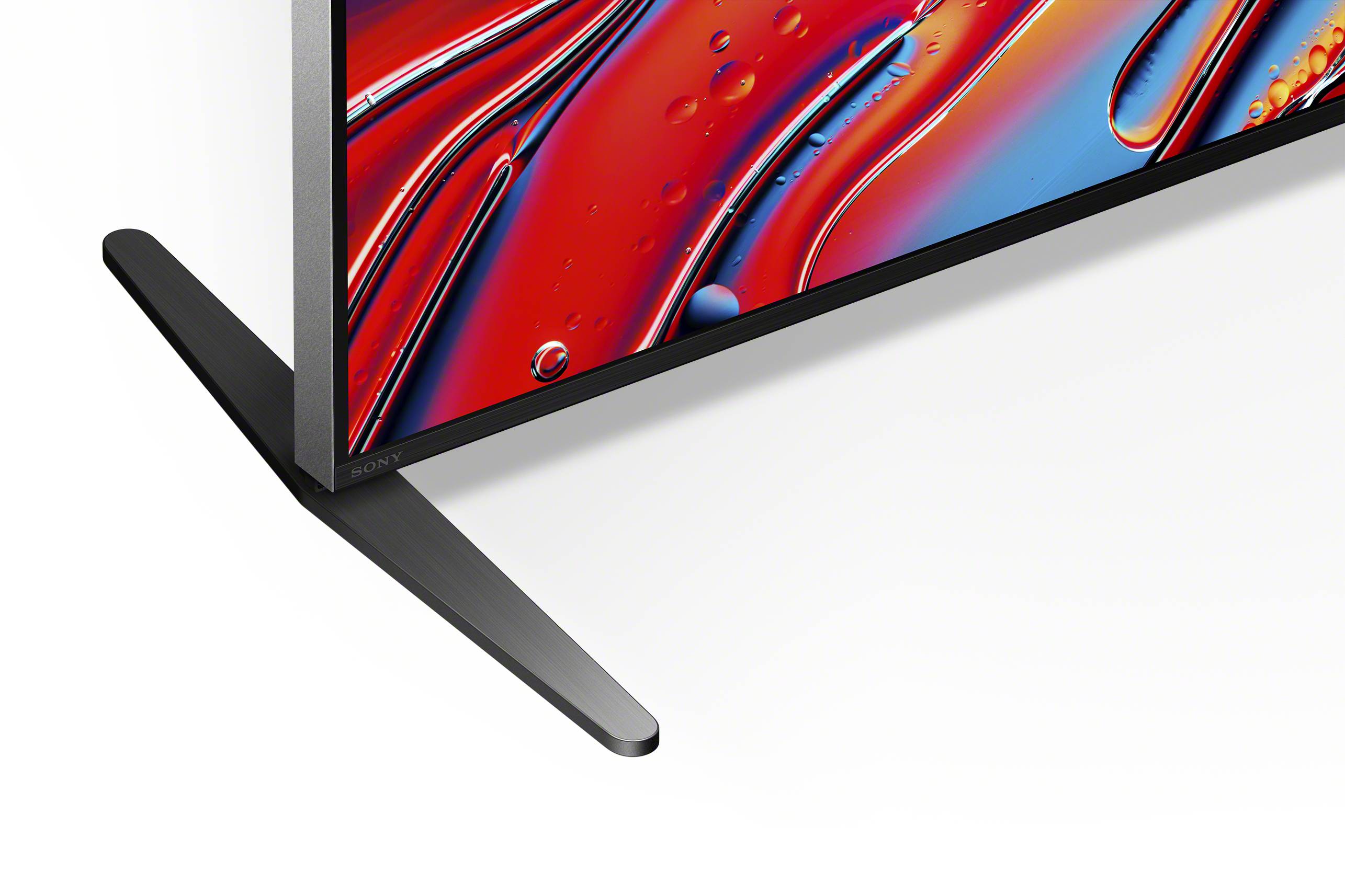 Primo piano di un televisore con base sottile e dal design moderno. Lo schermo mostra colori astratti luminosi.