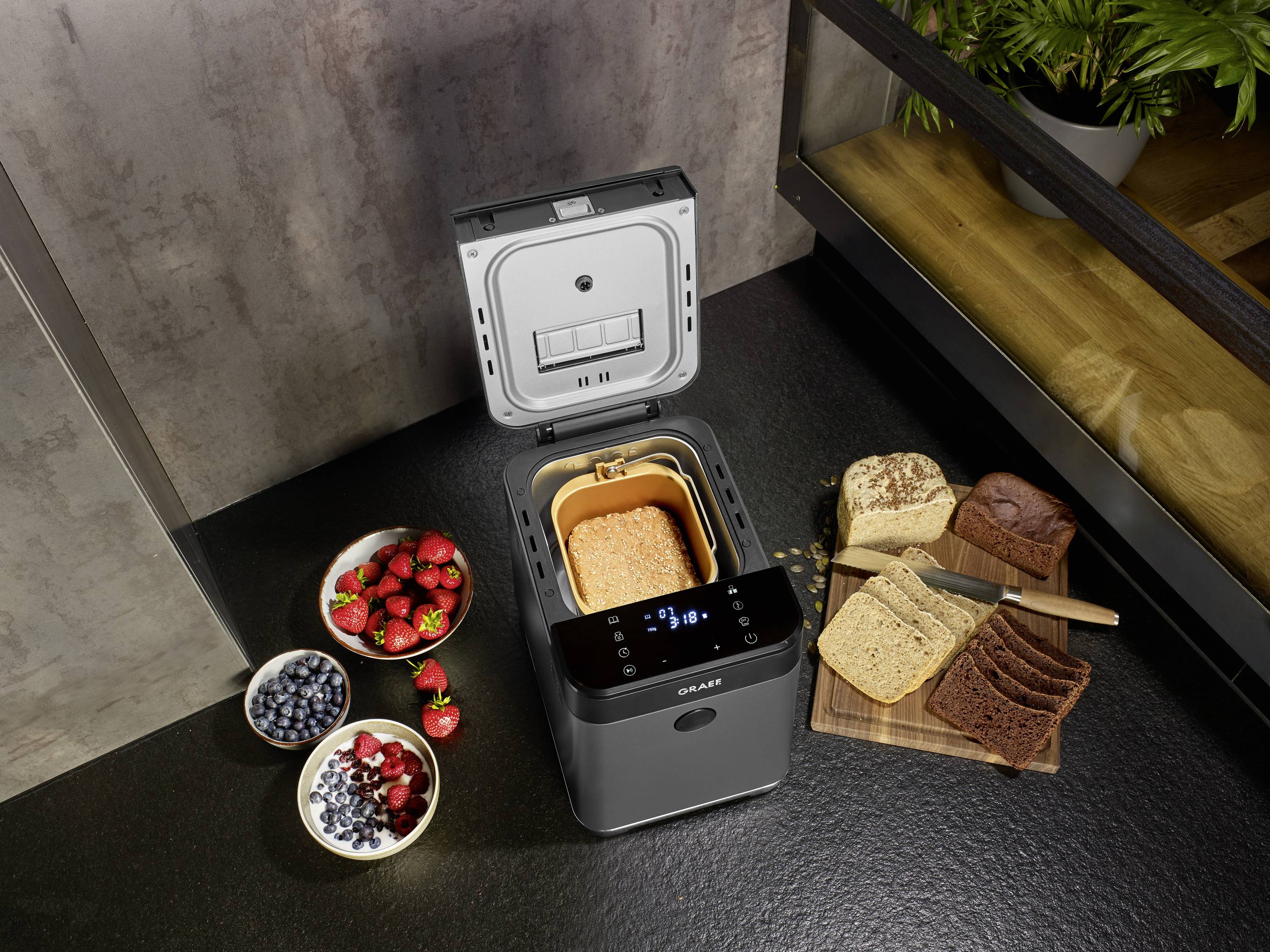 Una macchina per il pane con un pane appena sfornato nella sua forma, circondato da fragole fresche, mirtilli e pane tagliato.