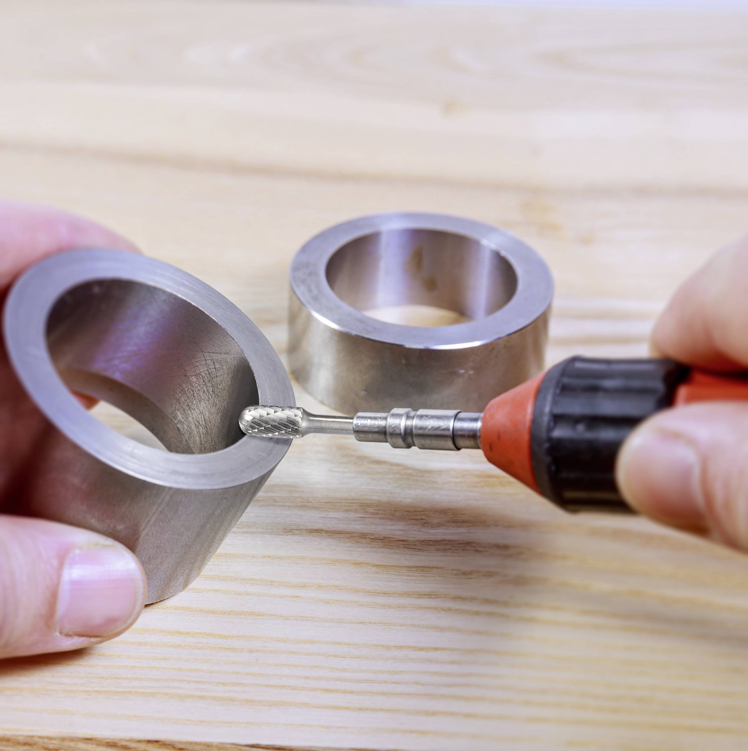 Una mano tiene un utensile vicino a due anelli metallici su una superficie di legno. Lo strumento viene utilizzato per levigare o lavorare gli anelli.
