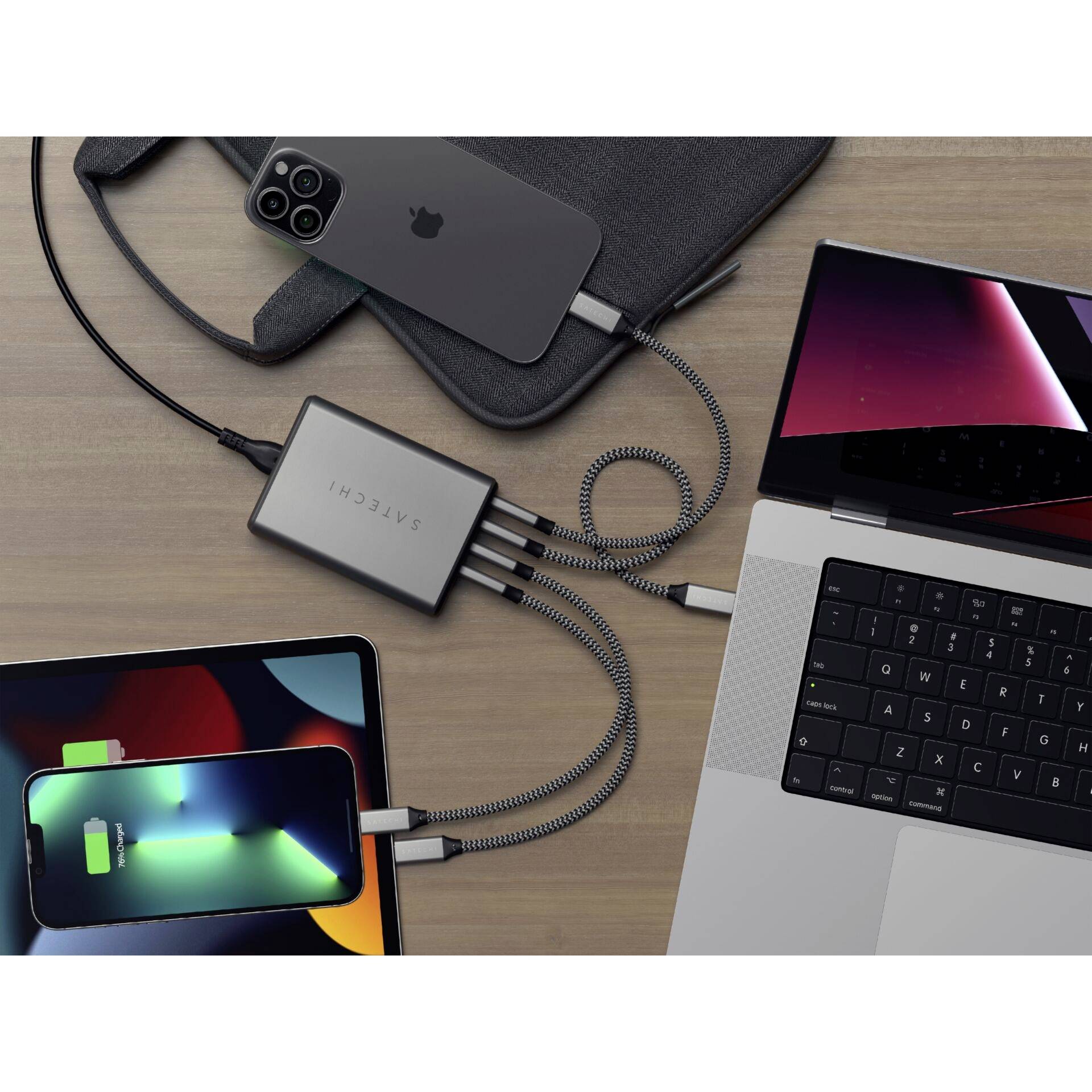 Diversi dispositivi come smartphone, laptop e tablet sono collegati a un hub USB centrale posizionato su un tavolo di legno.