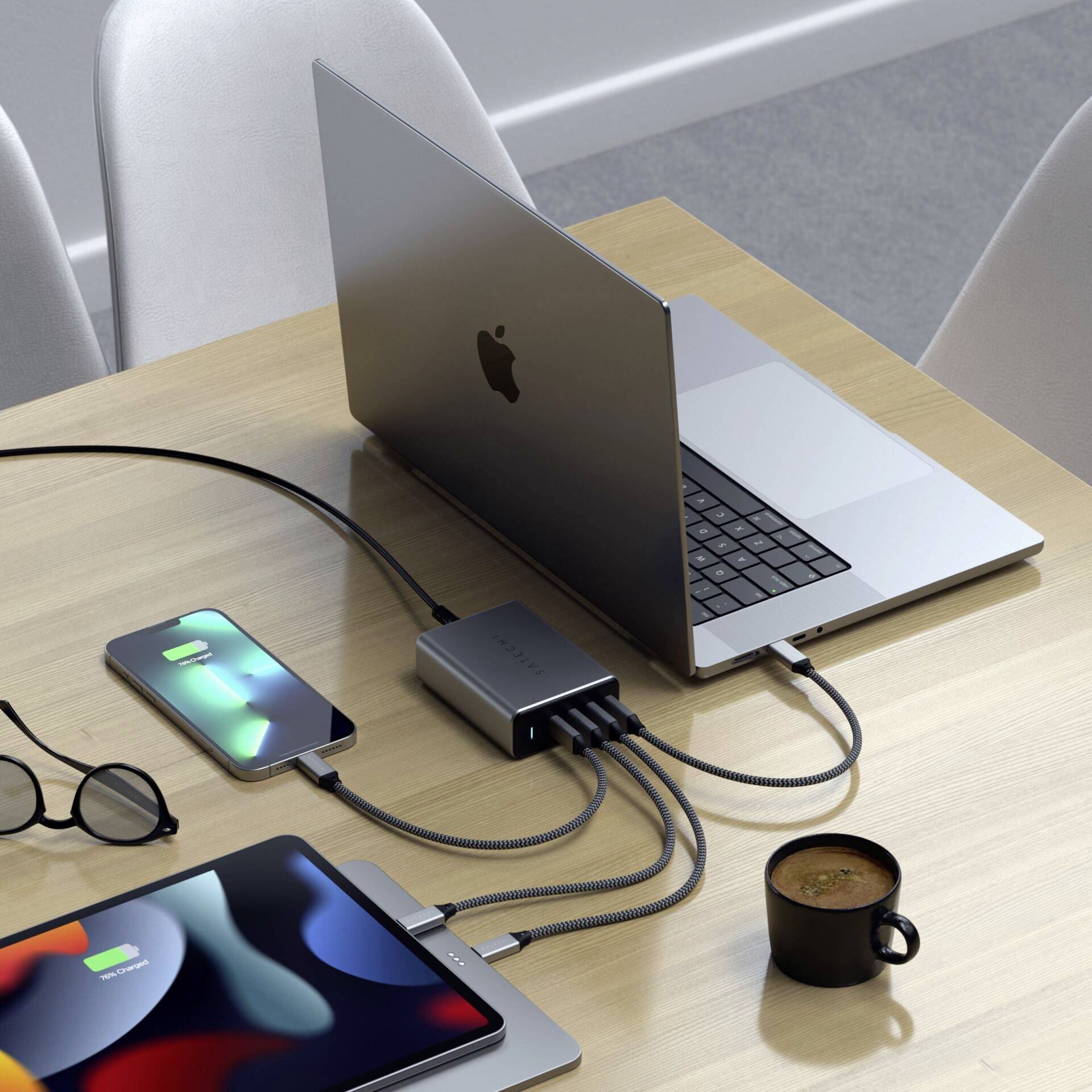 Un laptop su un tavolo è collegato tramite diversi cavi a uno smartphone e un tablet. Accanto si trovano un paio di occhiali e una tazza di caffè.