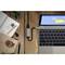 Laptop su un tavolo di legno, collegato a un hub USB; accanto un quaderno, una busta con sigillo di ceralacca, occhiali e gomma per cancellare.