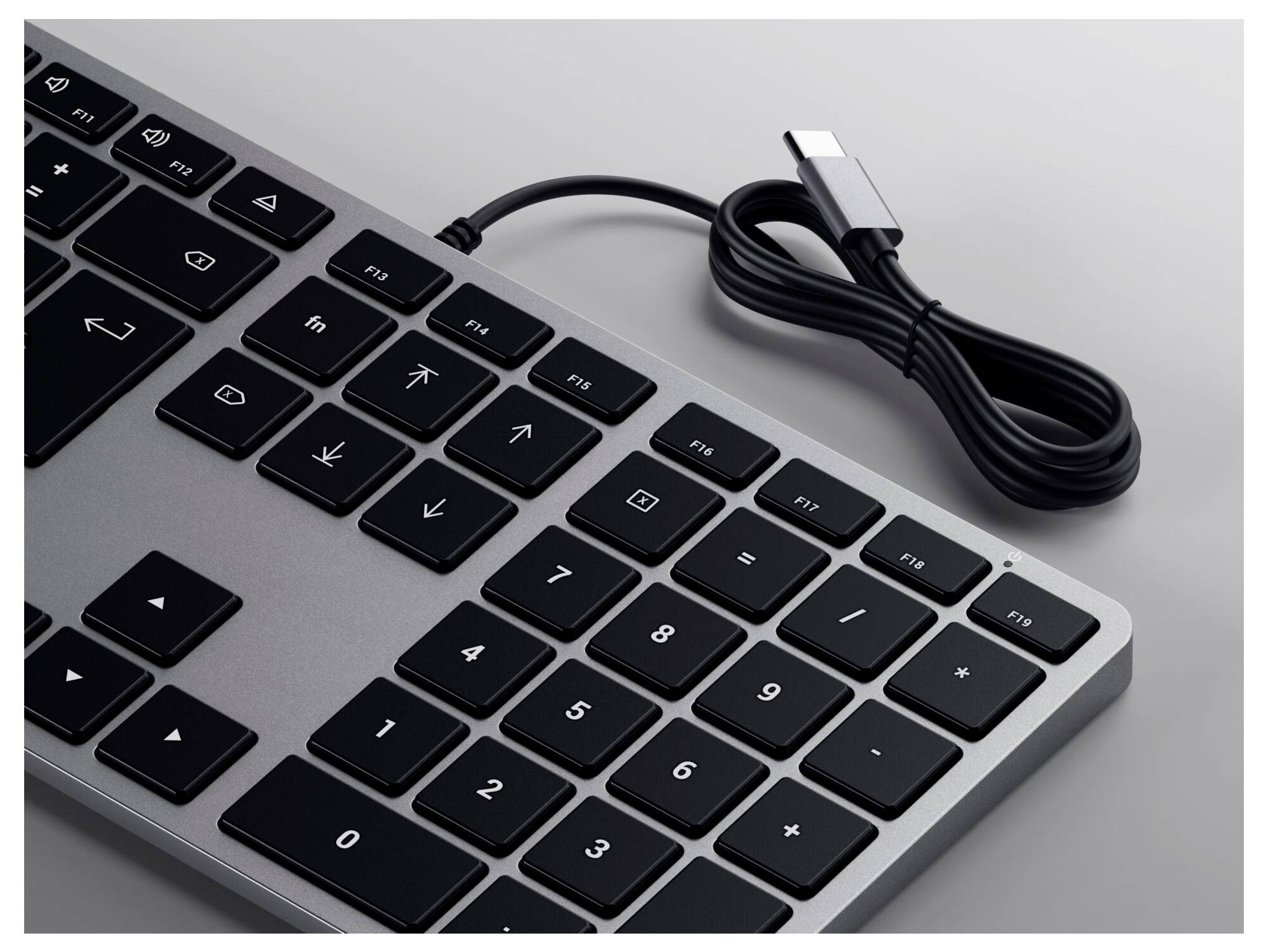 Tastiera USB nera con tastierino numerico su superficie grigia. Il cavo USB è attorcigliato e termina con un connettore USB-C.