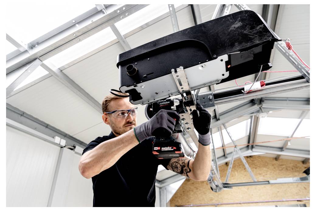 Un tecnico che indossa occhiali di sicurezza e guanti utilizza un attrezzo elettrico per installare o riparare un dispositivo industriale montato a soffitto in un laboratorio.