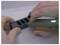 Una mano tiene un piccolo strumento elettrico, tagliando un pezzo rettangolare di materiale nero con più slot, su uno sfondo grigio chiaro.