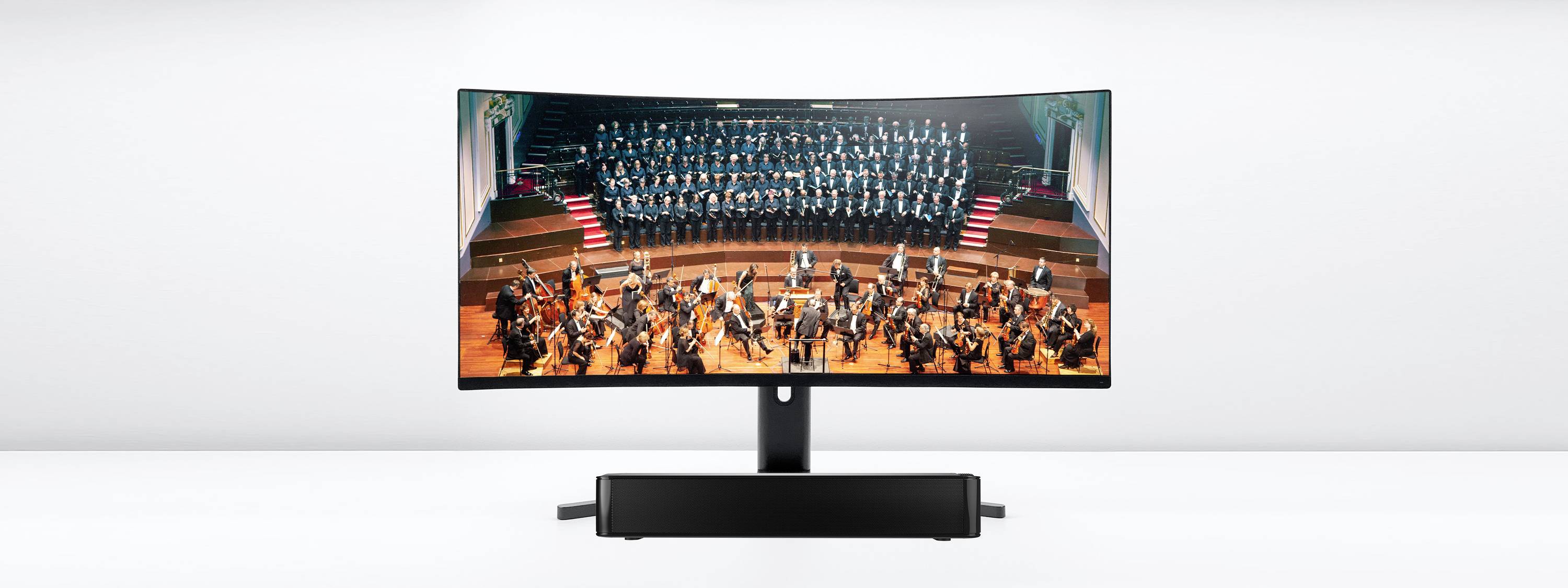 Un monitor mostra l'esibizione di un'orchestra con un coro sullo sfondo di un palcoscenico, con luci LED in primo piano.