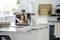 Un laptop su un bancone della cucina mostra una videochiamata con due persone anziane sorridenti che salutano con la mano sullo schermo.