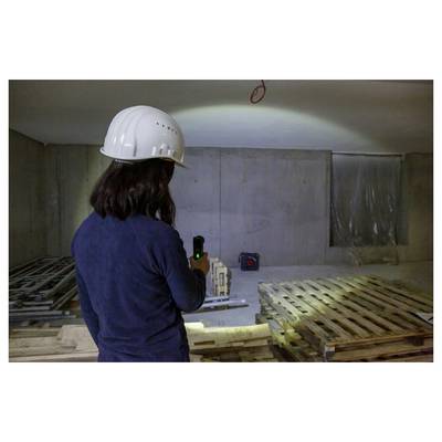 Un operaio con un casco utilizza un dispositivo portatile per ispezionare o misurare una stanza incompiuta con pallet e materiali da costruzione.
