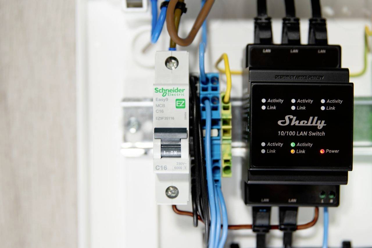 Quadro elettrico con interruttore magnetotermico Schneider e switch LAN Shelly. I cavi collegano i componenti.