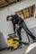 Un uomo in abiti da lavoro sta utilizzando un aspirapolvere giallo in un ambiente parzialmente allestito. Il soffitto è parzialmente scoperto, il pavimento è pulito.