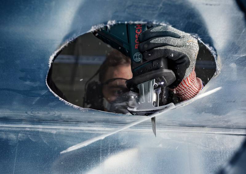 Una persona sta lavorando un pezzo di metallo ovale con un utensile elettrico. Occhiali protettivi e guanti garantiscono la sicurezza durante il lavoro.