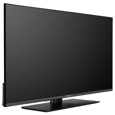 Un televisore piatto moderno su un piedistallo nero, fotografato da sinistra in diagonale. Lo schermo è spento.