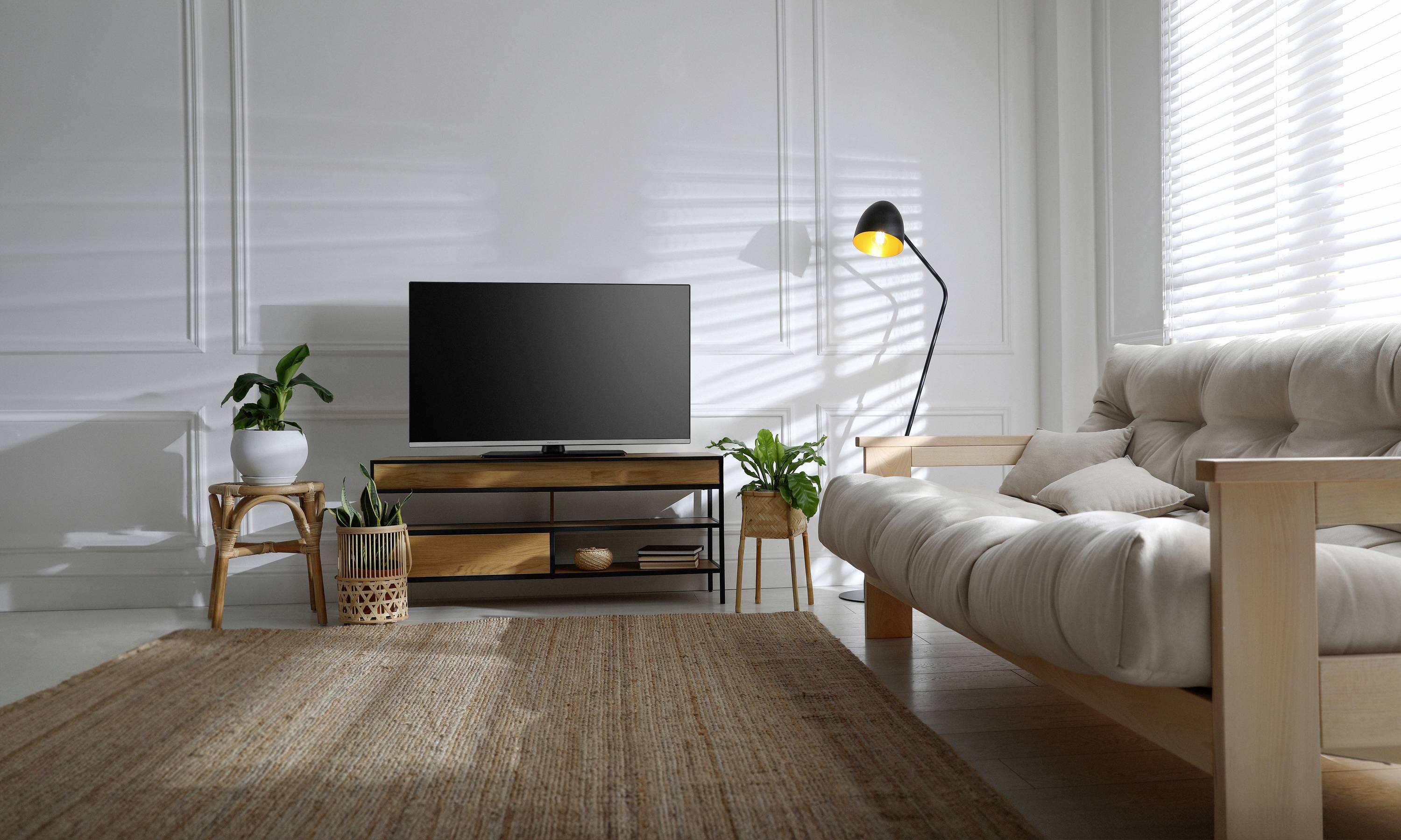 Un soggiorno moderno con un divano, un televisore su un supporto in legno e diverse piante. Illuminazione soffusa proveniente da una lampada da terra.