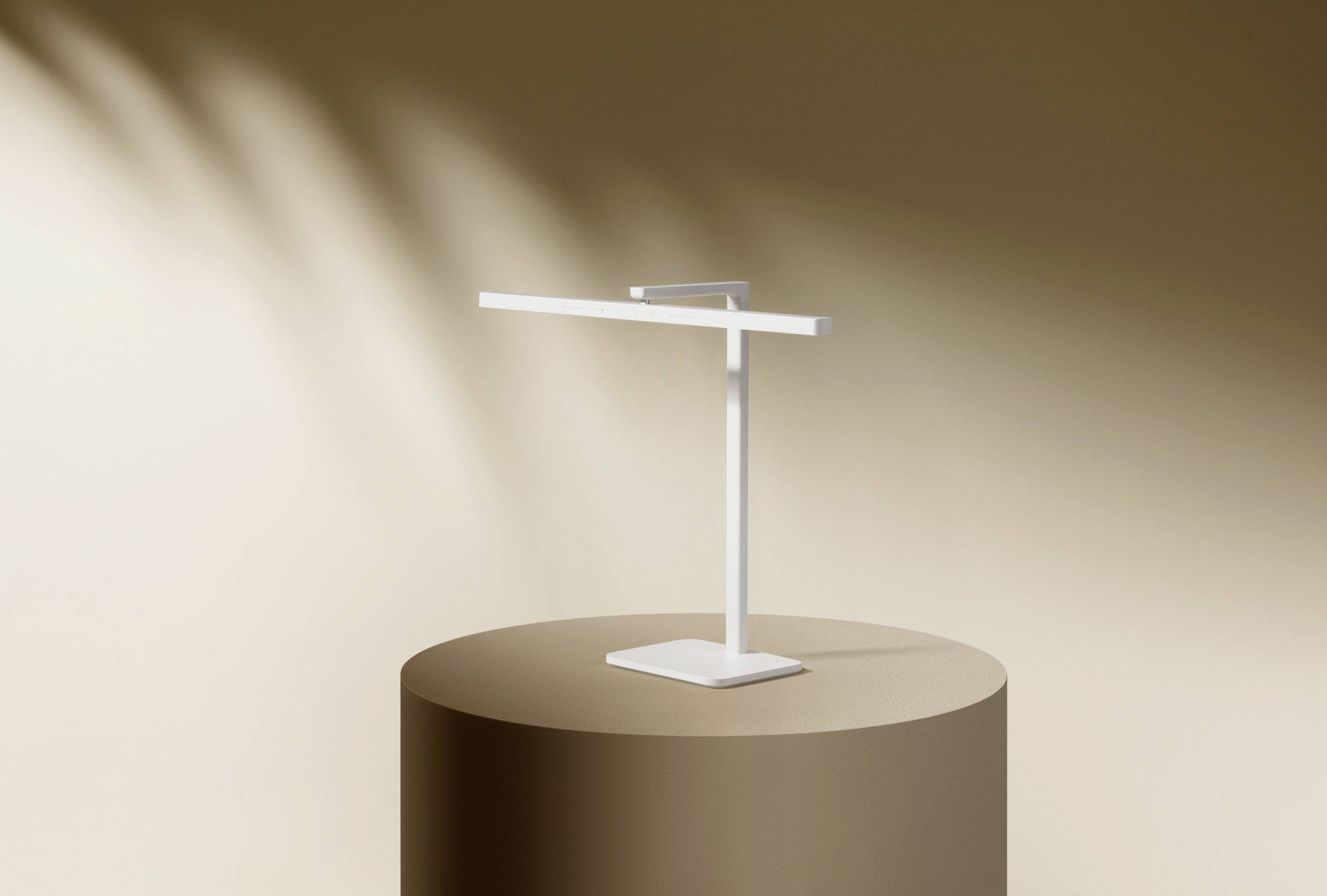 Una lampada da tavolo minimalista bianca è poggiata su un piedistallo cilindrico marrone su uno sfondo beige.