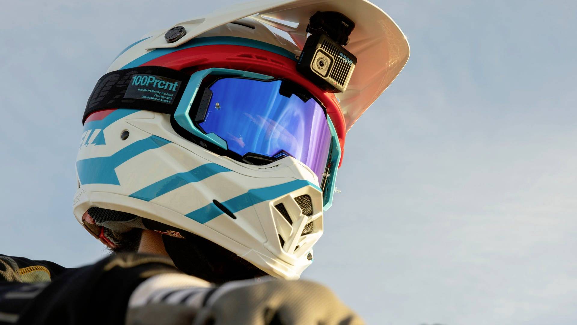 Un mountainbiker indossa un casco bianco con accenti blu e rossi, dotato di una telecamera, mentre guarda verso il cielo.