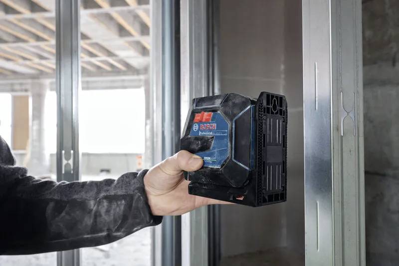 Una persona sta utilizzando un telemetro laser Bosch per misurare il telaio di una porta in un edificio parzialmente costruito.