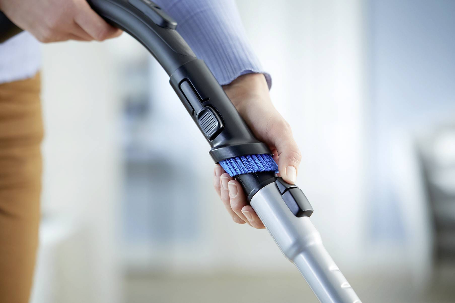 Una persona impugna un tubo dell'aspirapolvere con una spazzola blu, pronta a pulire una superficie.