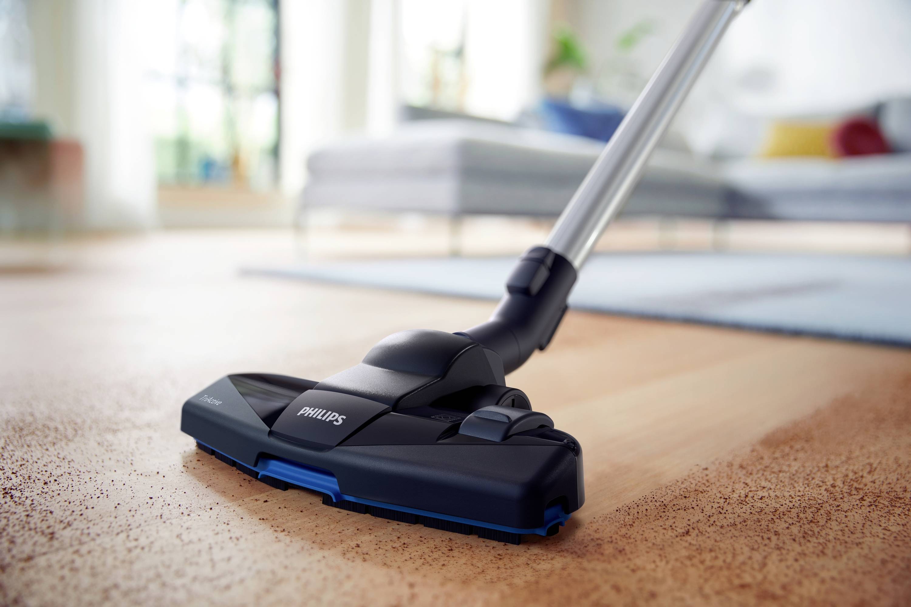 Aspirapolvere aspira lo sporco su un pavimento in legno in un appartamento luminoso e moderno, con un tappeto e un divano sullo sfondo.