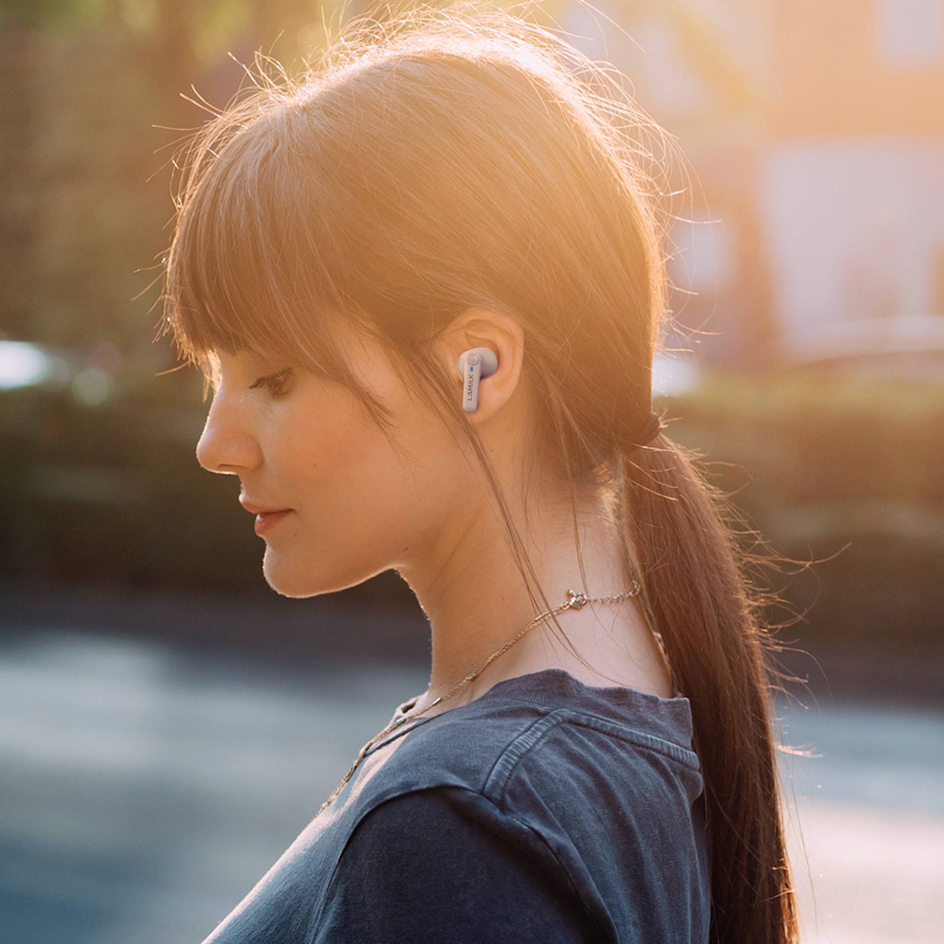 Una persona con capelli marroni indossa auricolari wireless ed è all'aperto durante il tramonto.