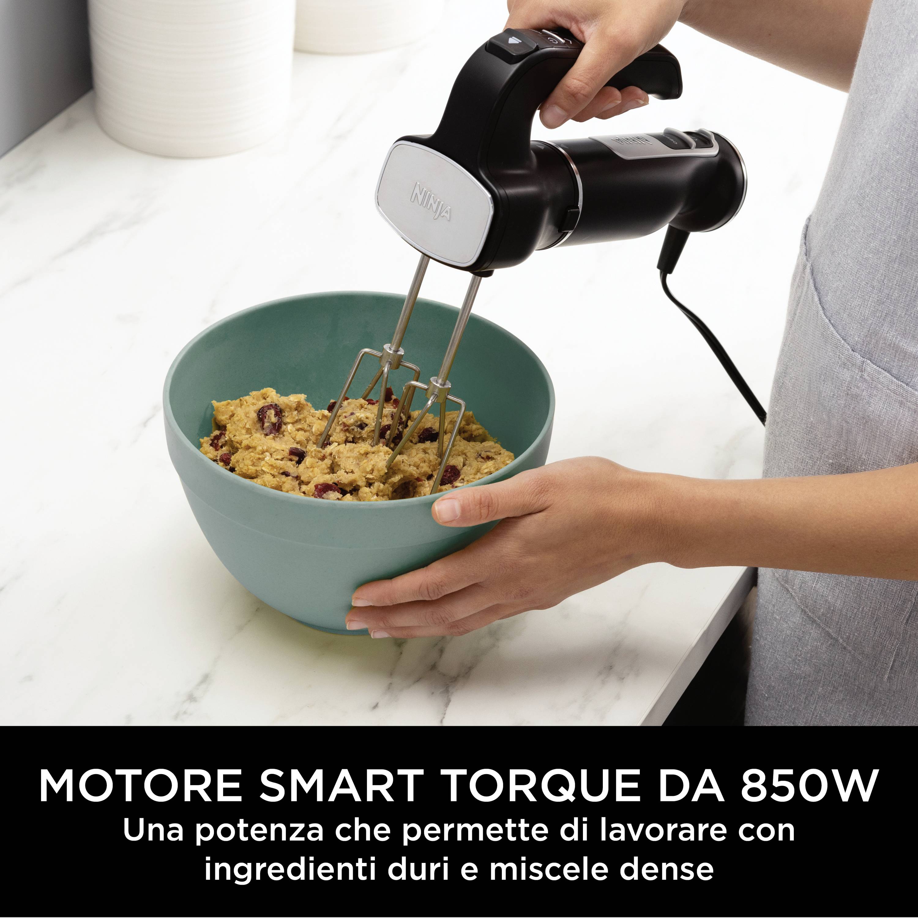 Una persona sta usando un mixer a mano per impastare in una ciotola. Testo: 'Motore smart torque da 850W', descrive la potenza del motore del mixer.