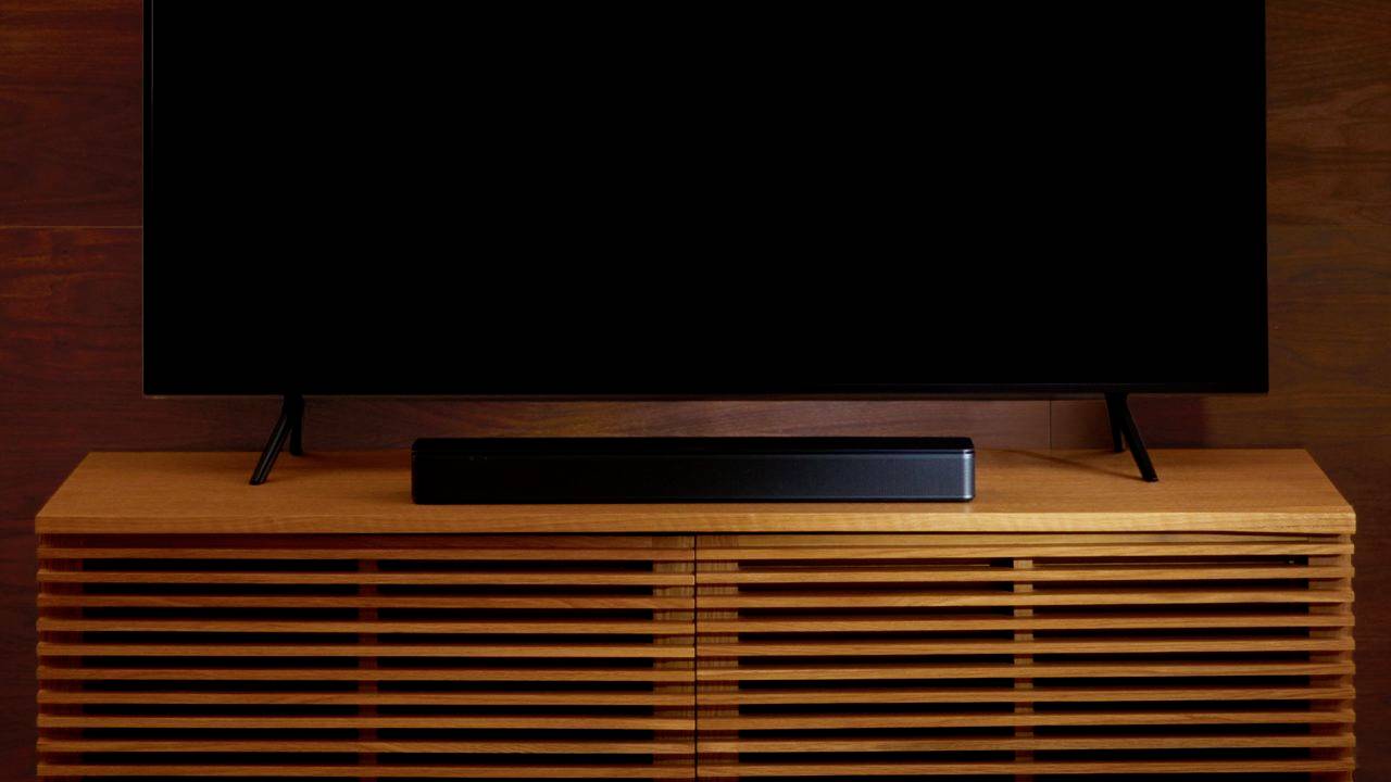 Un televisore a schermo piatto è posizionato su un mobile TV in legno con scanalature. Davanti al televisore c'è una soundbar nera.